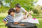 Man and son barbecuing with family in the background at park.jpeg